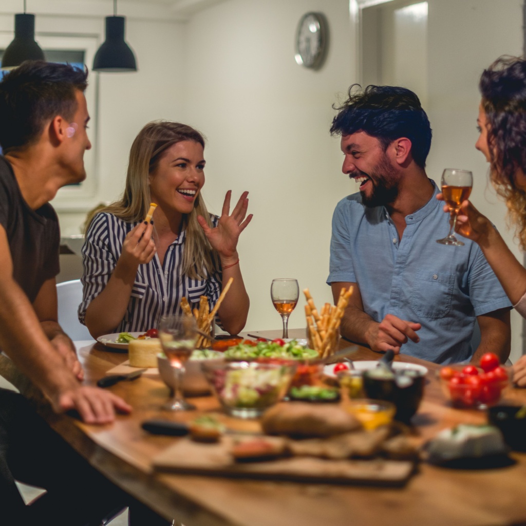 Group of friends sharing food and drinks, laughing, and chatting